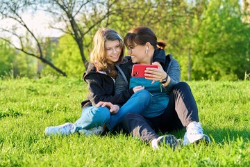 Naklejka na ściany i meble Mom and daughter looking together at smartphone screen, outdoor