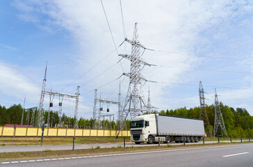 Towers, high-voltage power lines and a substation in the forest near the road. A truck drives past...
