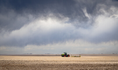 A tractor plowing a wheat field under a dramatic stormy sky on the Canadian prairies in Rocky View County Alberta Canada.