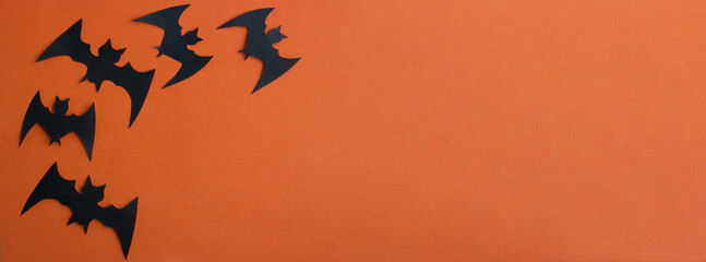 Black paper bats fly on an orange background. A banner for Halloween.Halloween Concept