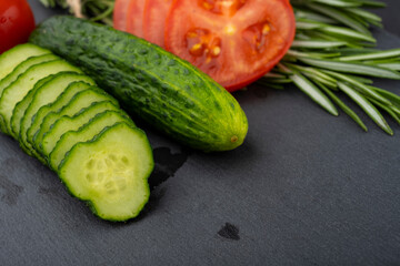 Vegetable table. Cucumbers, tomatoes and rosemary on a black table