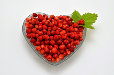 wild strawberries in a heart-shaped bowl on a white background close up