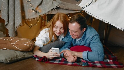 A young couple lies and communicates in a tent made of blankets and pillows in the bedroom. Romance