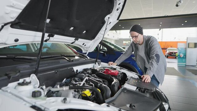 A man in a car showroom examines an engine under the hood.