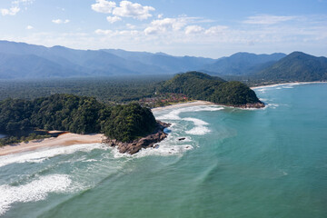 imagem aérea das praias do 
Engenho e da Juréia vistas de frente com a floresta tropical atrás, morros e céu azul 