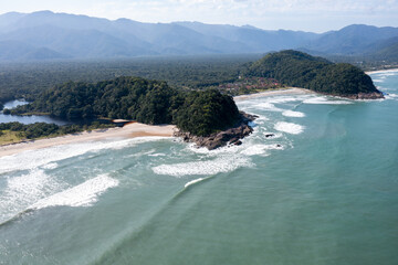 imagem aérea das praias do 
Engenho e da Juréia vistas de frente com a floresta tropical atrás, morros e céu azul 