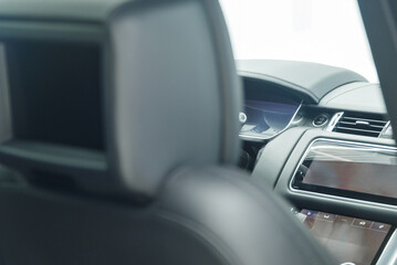 The car is inside. View from the back seat to the car control panel. The interior of a prestigious luxury modern car. TV display in the seat headrest.