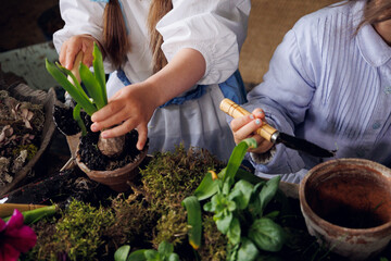 Two litlle sisters planting plant sets on wooden terrace. Two little baby girls of 3-years-old and 5-years-old in retro vintage dresses digging with a shovel soil and smiling. Child  fun and rest