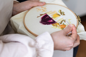Cross-stitch embroidering in progress. Young girl in linen clothes is doing handmade embroidery - obrazy, fototapety, plakaty