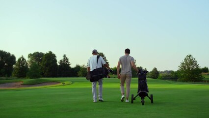 Rich golf players walking on field. Two active sportsmen carry equipment clubs. - Powered by Adobe