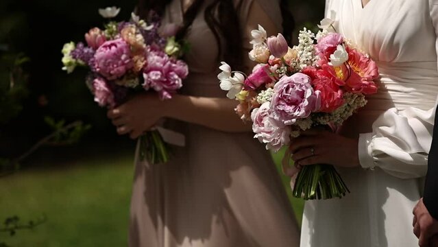 stylish wedding bouquet of flowers in hands of bride and bridesmaid outdoors at windy day. wedding ceremony of bride and groom.