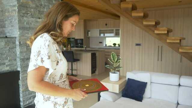 CLOSE UP: Pretty female feng shui practitioner using luo pan compass on location. Young woman doing feng shui analysis in home interior. Energy flow arrangements for balanced home living space design.
