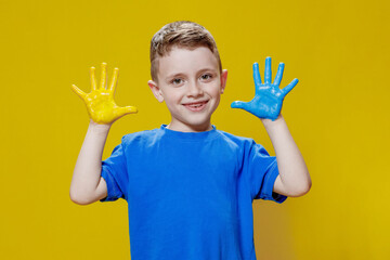 Little happy boy with painted palms in yellow and blue, the colors of the flag of Ukraine. Ukrainian creative preschooler