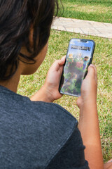 Fototapeta premium Child sitting on grass with Minecraft mobile game app on smartphone screen. Rio de Janeiro, RJ, Brazil. May 2022
