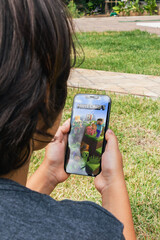 Fototapeta premium Child sitting on grass with Minecraft mobile game app on smartphone screen. Rio de Janeiro, RJ, Brazil. May 2022