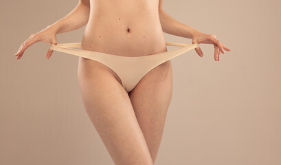 Cropped image of slender female body, belly in underwear isolated over grey studio background. Smooth legs