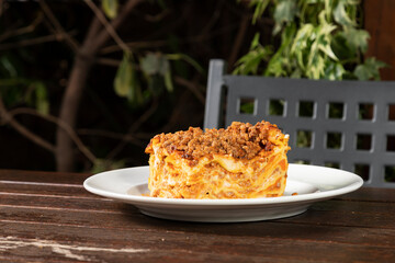 Traditional lasagna made with minced beef bolognese sauce and bechamel sauce topped. Lasagna bolognese on wooden table in a garden.