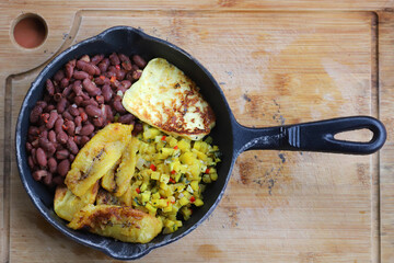 Top view of a cast Iron skillet with vegetarian meal in Costa Rica.  Beans, Sweet fried plantains, squash, fried cheese