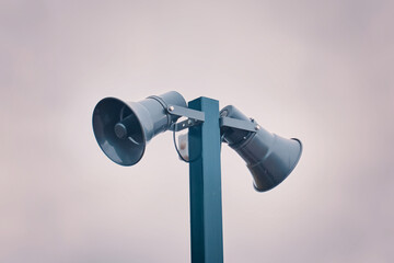Hazard warning system. Tall metal column with two gray loudspeakers against cloudy sky. Providing...