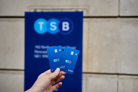 United Kingdom, Newcastle, May 27, 2022: New cards of TSB Bank on the background of their signage. A woman's hand holds the bank cards of TSB Bank.