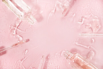 Close up of different pipette with pouring liquid essential oil on pastel pink background. Dropper glass with a falling drop of aromatherapy oil close-up.