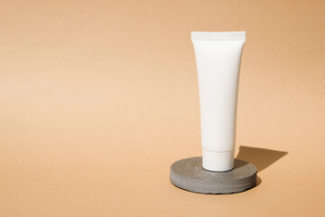 Beauty products display, grey stone podium on pastel beige background for skin care product presentation. Composition with a cosmetic white tube with copy space for text or design