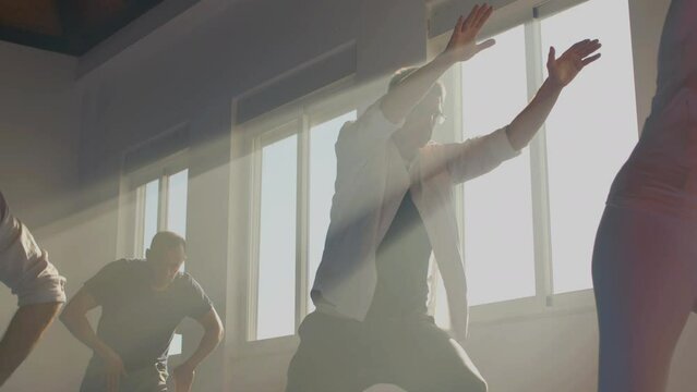 Senior men practicing tai chi in sunlight indoor. Medium shot of peaceful people performing slow movements in sunlight, meditating, doing sport together. Chinese martial arts, fitness concept