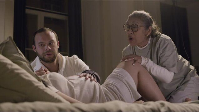 Elderly Asian doula delivering baby at home. Husband and midwife sitting next to pregnant woman, supporting, comforting and talking with her. Parenthood, medicine, pregnancy, occupation concept