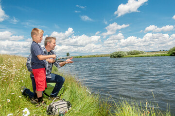 Fototapeta premium A father and son fishing together on a river bank on a beautiful summer day.
