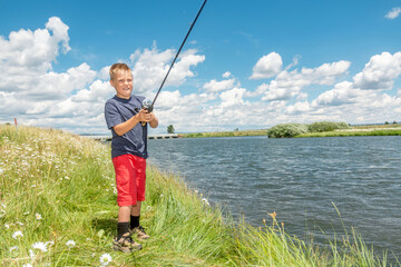 A young boy fishing on a river bank on a beautiful summer day.