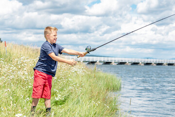 A young boy fishing on a river bank on a beautiful summer day.