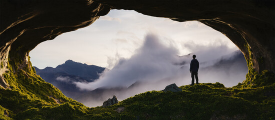 Adventurous Man standing in a rocky cave. Mountain Nature Landscape with clouds in background. Sunny Sunrise or Sunset. 3d Rendering Adventure Art.