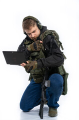 soldier, airsoft player in full gear works on a laptop in combat conditions. a man in headphones, a bulletproof vest, with a backpack and a belt, speaks, transmits information. White background.