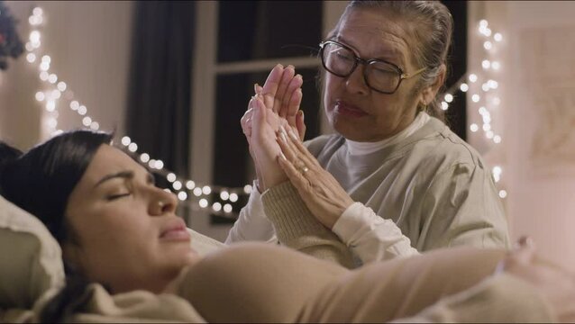 Asian doula sitting next ro pregnant woman and talking with her. Pregnant Caucasian woman feeling pain, preparing for childbirth, having contractions, stroking big belly. Motherhood, medicine concept