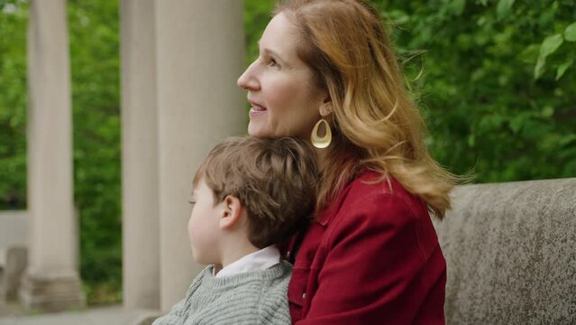 A mother is sitting with her young son on her lap, enjoying the breeze and rocking her boy