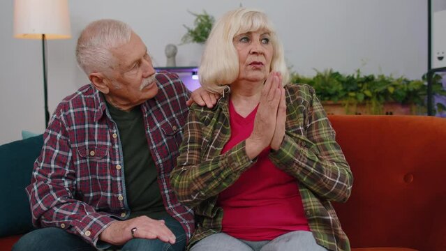 Senior Elderly Family Couple Grandparents Man Woman Pray With Hope, Looking Upward And Making Wish, Asking With Hopeful Imploring Expression, Begging Apology. Mature Grandmother Grandfather At Home