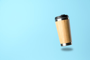 A reusable thermos cup for drinks flies in the air on a pastel blue background. Concept of plastic-free and zero waste living. Sustainable lifestyle. Personal takeaway beverages cup.