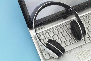 White and black wireless headphones with laptop computer on blue background with copy space for text.
