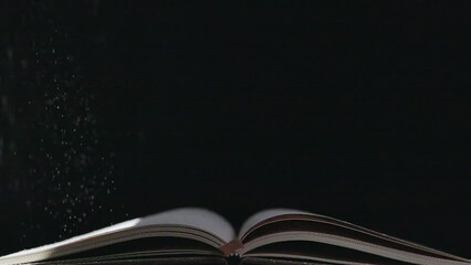 The book was opened with the dust falling on black background.

