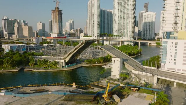 Boat driving on river in city, passing under double leaf bascule road bridge. Scene lit by setting sun. Miami, USA