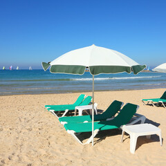 Sandy beach with sun umbrella and green lounges