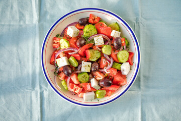 Greek salad with feta cheese, olives, tomato, cucumber and red onion, healthy vegeterian mediterranean diet food, low calories eating. Blue fabric background, top view