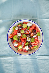 Greek salad with feta cheese, olives, tomato, cucumber and red onion, healthy vegeterian mediterranean diet food, low calories eating. Blue fabric background, top view