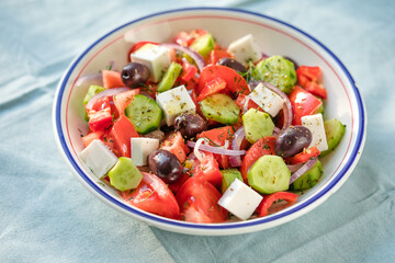 Greek salad with feta cheese, olives, tomato, cucumber and red onion, healthy vegeterian mediterranean diet food, low calories eating. Blue fabric background, top view