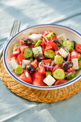 Greek salad with feta cheese, olives, tomato, cucumber and red onion, healthy vegeterian mediterranean diet food, low calories eating. Blue fabric background, top view