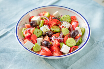 Greek salad with feta cheese, olives, tomato, cucumber and red onion, healthy vegeterian mediterranean diet food, low calories eating. Blue fabric background, top view