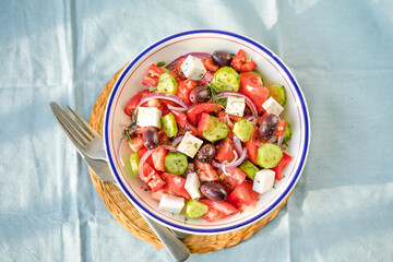 Greek salad with feta cheese, olives, tomato, cucumber and red onion, healthy vegeterian mediterranean diet food, low calories eating. Blue fabric background, top view