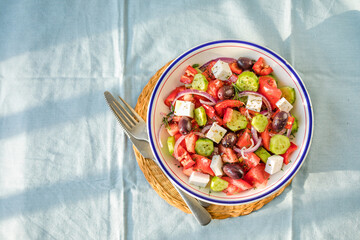 Greek salad with feta cheese, olives, tomato, cucumber and red onion, healthy vegeterian mediterranean diet food, low calories eating. Blue fabric background, top view