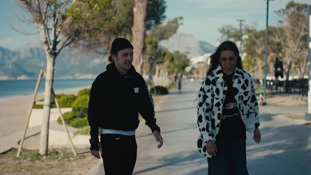 Happy man beautiful woman, riding on skateboard. Young beautiful couple walking at seaside, skateboarding