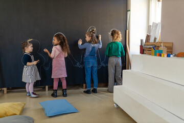 Group of little girls posing in front of blackboard wall paintings indoors in playroom.